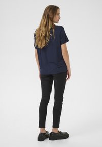 T-shirt bleu marine à manches courtes avec une coupe décontractée, associé à un jean skinny noir et des chaussures noires imposantes, vu de derrière.