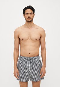Shorts de bain à carreaux noir et blanc avec une taille élastique, en tissu léger et à coupe décontractée, portés par un modèle masculin.