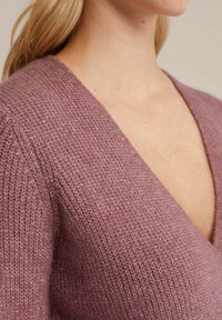 Stickad tröja i dammrosa, med djup V-ringning, texturerat tyg med ett subtilt mönster och mjukt, lätt material.
