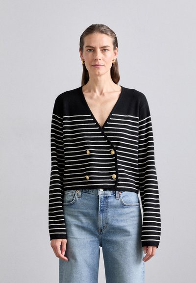 Black and white striped cardigan with a deep V-neck, double breasted gold buttons, and long sleeves, paired with light blue jeans.