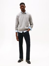 Gray sweatshirt with crew neckline, layered over a light blue shirt, paired with dark denim pants and black loafers. Simple and classic design.
