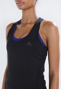 Camiseta sin mangas atlética negra con un diseño ajustado, que cuenta con una capa interior de color azul oscuro, tirantes ajustables y un logo de Adidas en relieve.