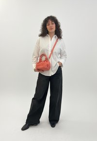 Lososová kabelka s naťahovaným vrchom a krátkymi rúčkami, nosená k bielej košeli na gombíky a širokým čiernym nohaviciam. Hladké textúry látky.