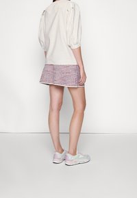 Ljusbeige topp med puffärmar och spetskrage, i kombination med en kort röd och vit rutig kjol samt pastellfärgade sneakers.