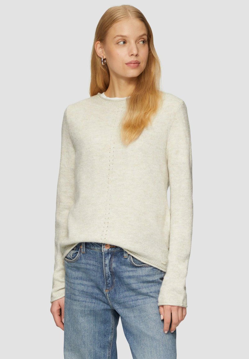 Lichtbeige gebreide trui met lange mouwen, ronde halslijn en een subtiele verticale stiksel detail in het midden. Gepaard met blauwe jeans.