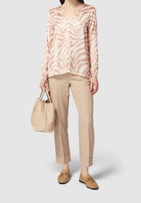 La blusa presenta un motivo a onde bianco e rosa chiaro, maniche lunghe e scollatura a V. Abbinata a pantaloni beige su misura e mocassini color cammello.