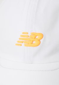 Hvid kasket med en broderet orange "New Balance"-logo, der har en glat tekstur og struktureret design.