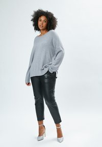 Maglione grigio oversize con maniche lunghe, abbinato a pantaloni in pelle nera e scarpe con tacco argentate dal finish scintillante.