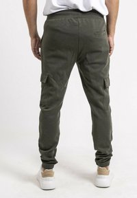 Pantalons cargo vert olive au design ajusté, texture côtelée, poches latérales et poignets élastiques, associés à des baskets blanches.