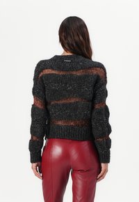 Knit black sweater with orange metallic stripes and ribbed texture. Features a rounded neckline and a cropped fit. Brand logo displayed at the back.