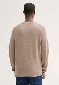 Beige stickad tröja med rund hals, raglanärmar och ribbstickade muddar. Mjuk textur med en subtilt blandad färg genom hela plagget.