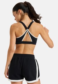 Sostenedor deportivo negro con acentos blancos y tirantes cruzados en la espalda, combinado con pantalones cortos negros que tienen rayas laterales blancas. Tejido suave y elástico.