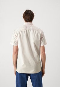 Lichtroze shirt met korte mouwen, een achterpas, subtiele textuur en een afgeronde zoom, gecombineerd met loszittende blauwe spijkerbroek.