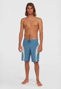 Blaue Boardshorts mit einem Kordelzugbund, die mit hellgrünen und weißen Wellenmustern versehen sind. Hergestellt aus leichtem, schnelltrocknendem Material.