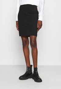 Černá tužková sukně s přizpůsobeným střihem, hladkou texturou a pasovým páskem. Kombinováno s černými kotníkovými botami.