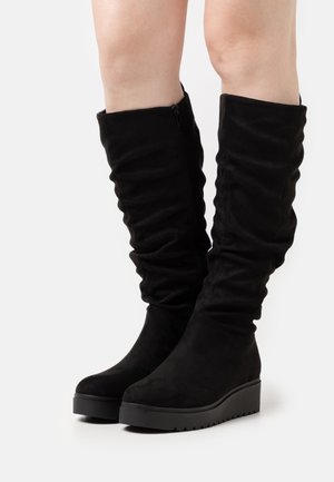 Bottes noires montantes jusqu'au genou avec un design décontracté, fabriquées en daim doux, dotées d'une semelle plateforme épaisse et d'une fermeture éclair latérale.