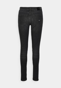 Vaqueros skinny de mezclilla negra con una textura suave. Presenta dos bolsillos traseros y un pespunte sutil. Cintura alta con un parche de logo en la cinturilla.