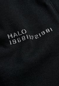 Sort stof med hvid stenciltekst "HALO 1968 1972 1981" arrangeret diagonalt over overfladen.