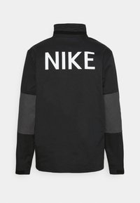 Black jacket with a high collar. Features large white "NIKE" logo on the back, gray accents on sleeves, and a smooth fabric texture.