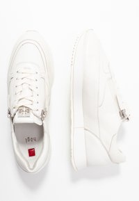 Valkoiset nahkalenkkarit, joissa on sileä pinta, pyöreä kärki ja sivulla vetoketjuyksityiskohta. Kenkässä on nauhakiinnitys ja pehmustettu kieli.