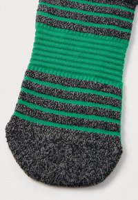 Πλεκτή κάλτσα με πράσινες και σκουρόγκρινες ρίγες, με ραβδωτή υφή γύρω από το μεσαίο τμήμα, σε λευκό φόντο.