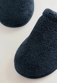 Weiche, dunkelblaue Hausschuhe mit einer plushigen, strukturierten Oberfläche und abgerundeter Form. Sie verfügen über eine gepolsterte Sohle und ein niedriges, geschwungenes Knöchel-Design.