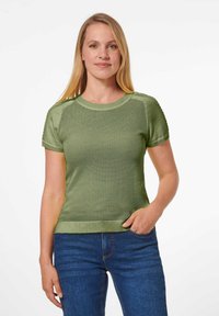 Kurzärmliges Stricktop in Hellgrün mit strukturiertem Gewebe und glatten Ärmeln. Kombiniert mit blauen Jeans, was einen lässigen Schnitt und Stil zeigt.