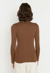 Brun ribbad långärmad topp med hög hals, featuring en figurnära siluett och en något böjd nederkant. Mjuk textur, minimal detalj.