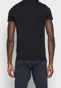 Camiseta de algodón de manga corta negra, con cuello redondo y textura suave. La vista trasera muestra un diseño sencillo sin gráficos.