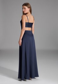 Abito navy con un corpetto aderente in paillettes e una gonna in satin fluida. Spalline sottili regolabili e vita che accentuano la silhouette.