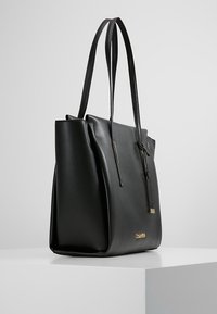 Black leather tote bag with a smooth texture, featuring long handles, a structured shape, and a gold logo accent on the side.