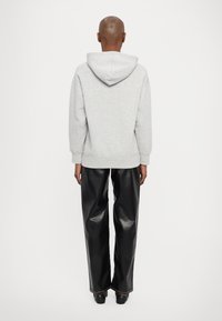 Felpa grigia con cappuccio e vestibilità rilassata, abbinata a pantaloni larghi in pelle nera. La felpa presenta polsini e vita a costine.