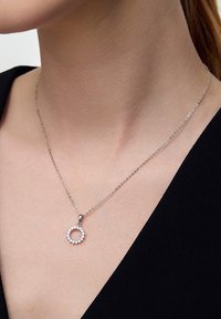 Srebrny naszyjnik łańcuszkowy z okrągłym wisiorkiem zdobionym małymi, błyszczącymi kamieniami, osadzonymi w delikatnym wzorze.