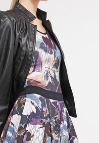 Veste en cuir noir sur une robe multicolore avec des motifs abstraits ; la robe présente un corsage ajusté et une jupe évasée.