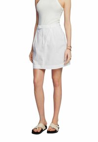 Falda de lino blanca con cintura ajustada, pliegues y bolsillos laterales. Combinada con una camiseta sin mangas ligera y sandalias de color neutro.