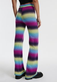Multicolore flare broek met horizontale strepen in roze, paars, blauw en geel. Zacht materiaal met een brede tailleband en een losse pasvorm.