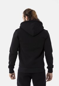 Schwarzer Fleece-Hoodie mit großer Kapuze, Rippbündchen und Saum. Glatte Textur mit minimal sichtbaren Nähten. Rückansicht zeigt die Passform.
