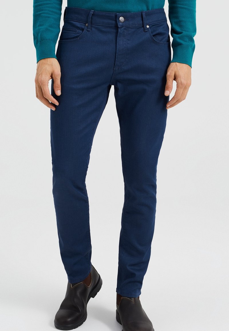 Navy blue slim-fit jeans with a classic five-pocket design. Made of denim, featuring a silver button closure and subtle texture.