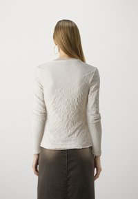 Svetle béžový dlouhý rukáv top s texturovaným diamantovým vzorem, měkká tkanina, kulatý výstřih a slim fit, spárován s tmavě hnědou sukní.