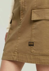 Gonna in cotone khaki con tasche cargo, dal taglio dritto e etichetta G-Star Originals. Tessuto testurizzato con dettagli di cucitura visibili.
