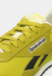 Žute Reebok tenisice s debelim vezicama, gornjište od antilopa i mrežice, crna bočna pruga i vidljivi Reebok logo s oznakom britanske zastave.