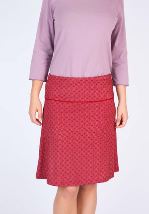 Roter Rock mit einem wellenförmigen Muster, festem Bund und A-Linien-Silhouette. Kombiniert mit einem helllila Oberteil und Dreiviertelärmeln.