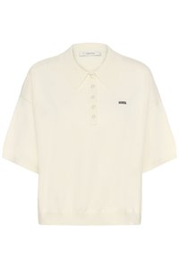 Krēmkrāsas īsroku adīta polo krekls ar pieciem pogām un mazu melnu izšūtu logotipu kreisajā krūtīs.