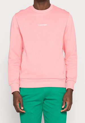 Roze sweatshirt van zacht materiaal, met een ronde halslijn en ribgebreide boorden. Een witte "Calvin Klein"-logo is in het midden van de borst geplaatst.