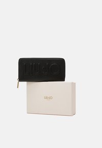 Cartera de cuero negro con el logo emblema "LIU·JO" en relieve. Cuenta con una cremallera y herrajes en tono dorado. Presentada en una caja beige con texto dorado.