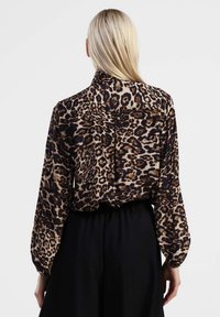 Blusa con stampa leopardata, maniche lunghe, dettaglio sul retro e una texture morbida. Abbinata a pantaloni neri con vita elasticizzata.