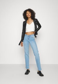 Jaqueta de motociclista preta em couro, top cropped branco com padrão texturizado, jeans de perna reta azul claro e sapatos pretos slip-on.