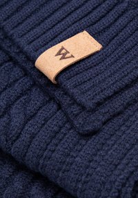 Námořnická pletená šála s žebrovanou texturou a koženou cedulkou s vyrytým písmenem "W". Měkký, teplý materiál s hřejivým vzhledem.