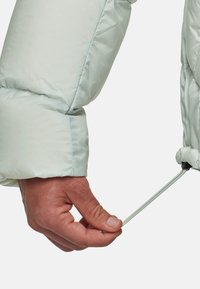 Handmatig aandraaien van de verstelbare trekkoord bij de manchette van de mouw van een lichtgrijze pufferjack.