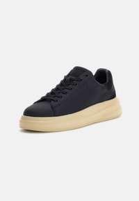 Sneaker nera realizzata in materiale liscio, con una spessa suola color crema, punta rotonda e un classico design con lacci, arricchita da un branding sottile sul lato.